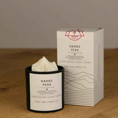 A white wax replica candle of Hahns Peak next to a white box with red and black lettering.