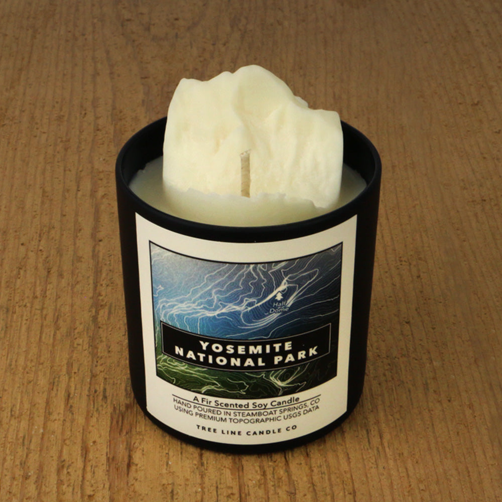 A white soy wax replica candle of Half Dome in a round, black glass.