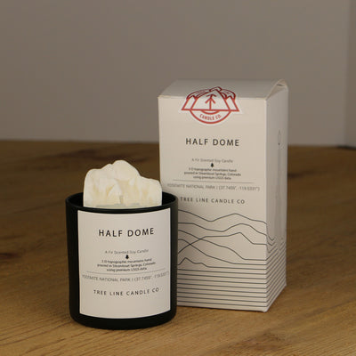 A white wax replica candle of Half Dome next to a white box with red and black lettering.