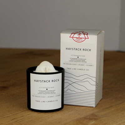 A white wax replica candle of Haystack Rock next to a white box with red and black lettering.