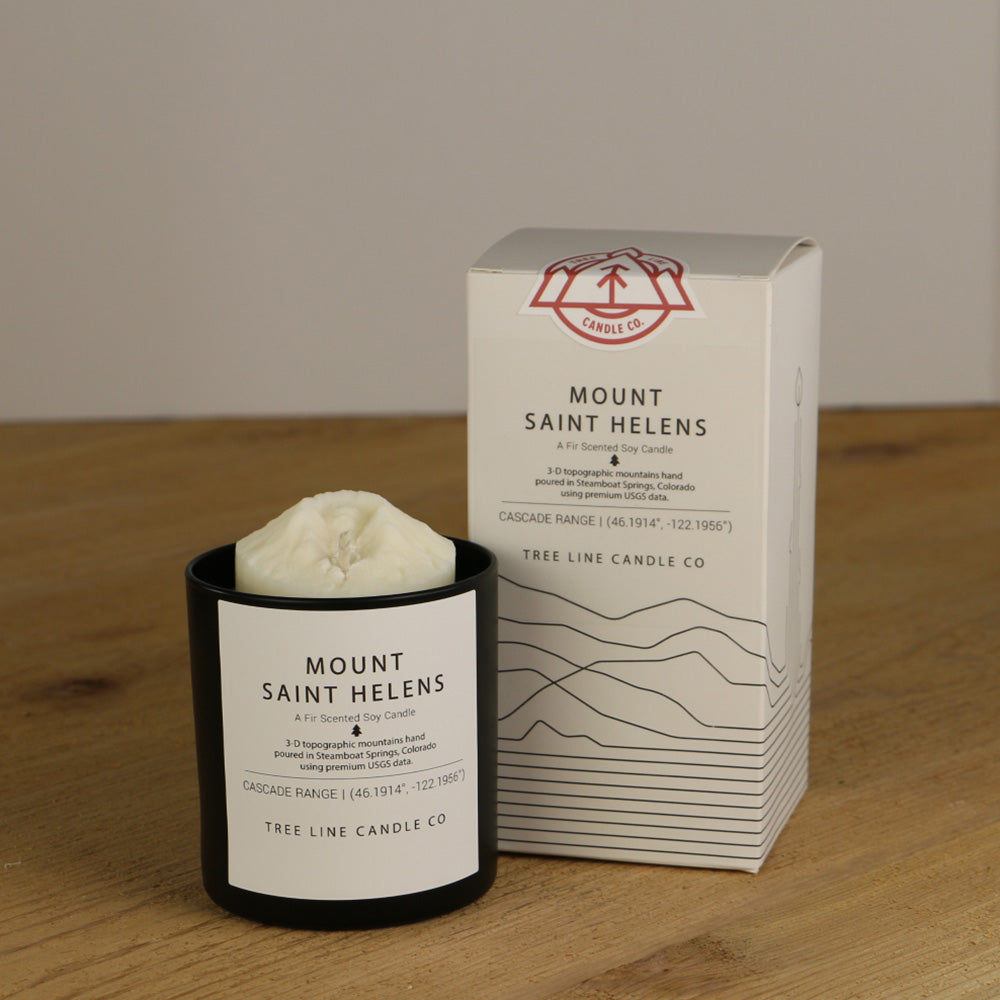 A white wax replica candle of Mount Saint Helens next to a white box with red and black lettering.