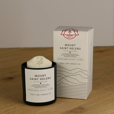 A white wax replica candle of Mount Saint Helens next to a white box with red and black lettering.