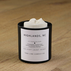  A white soy wax replica candle of Highlands, N.C. in a round, black glass.