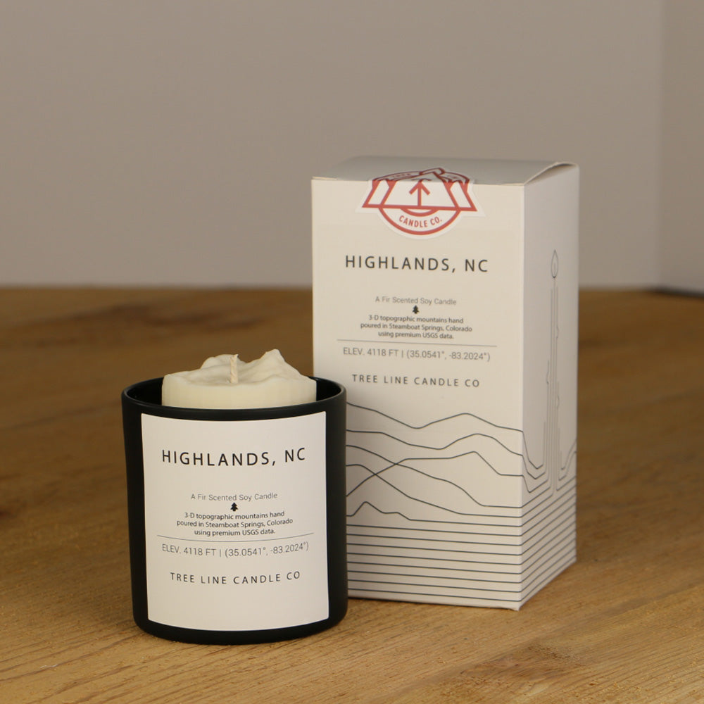 A white wax replica candle of Highlands, NC summit next to a white box with red and black lettering.