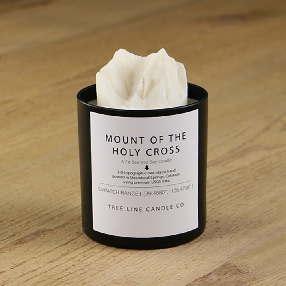 A white soy wax replica candle of Mount Of The Holy Cross in a round, black glass.