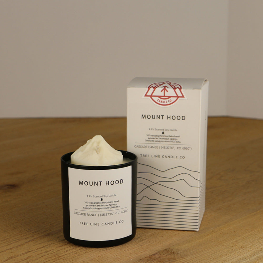 A white wax replica candle of Mount Hood next to a white box with red and black lettering.