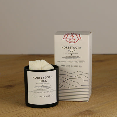 A white wax replica candle of Horsetooth Rock summit next to a white box with red and black lettering.