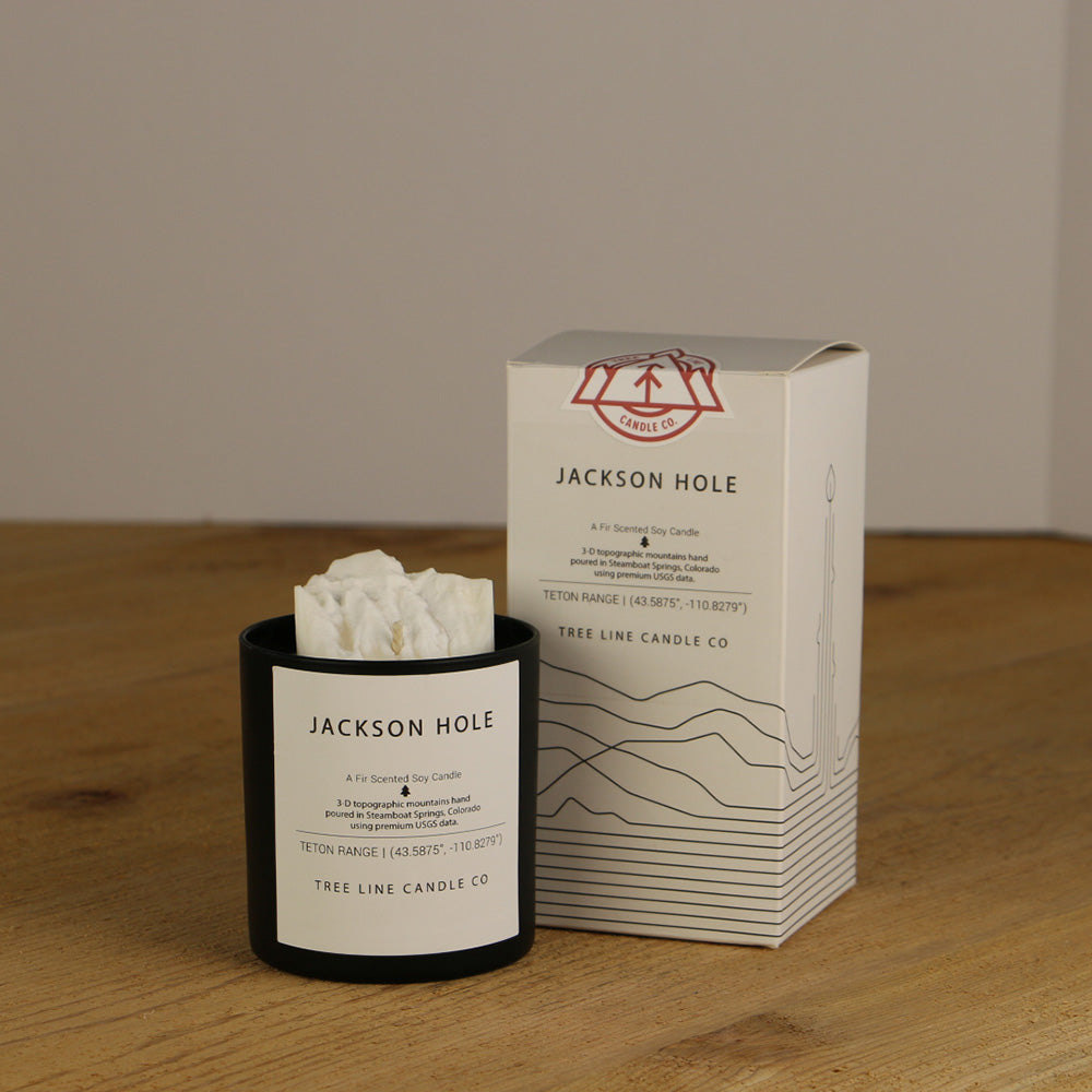 A white wax replica candle of Jackson Hole summit next to a white box with red and black lettering.