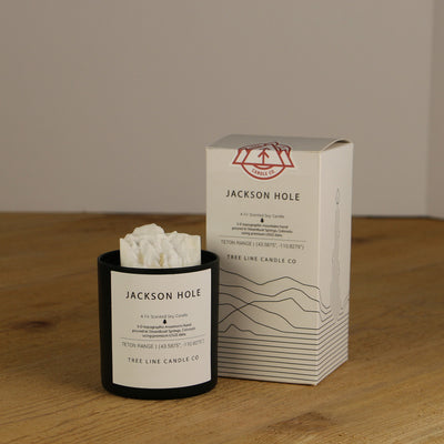 A white wax replica candle of Jackson Hole summit next to a white box with red and black lettering.