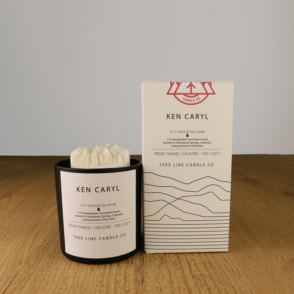 A white wax candle named Ken Caryl is next to a white box with red and black lettering.