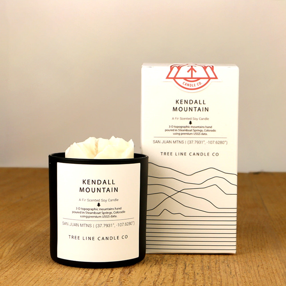 A white wax candle named Kendall Mountain is next to a white box with red and black lettering.