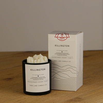 A white wax replica candle of Killington summit next to a white box with red and black lettering.