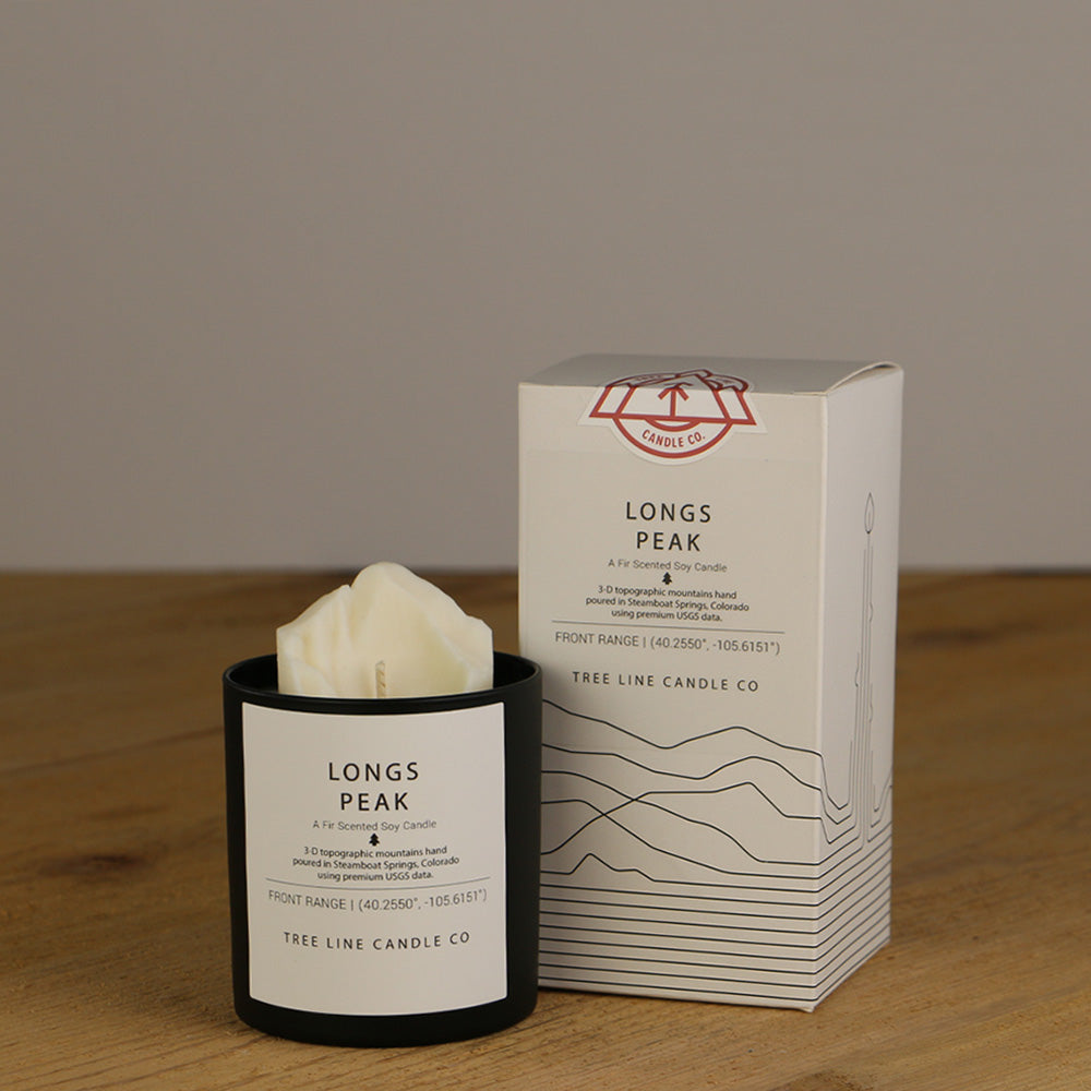 A white wax replica candle of Longs Peak next to a white box with red and black lettering.