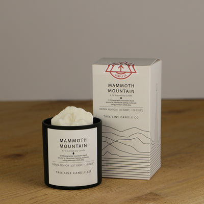 A white wax replica candle of Mammoth Mountain next to a white box with red and black lettering.