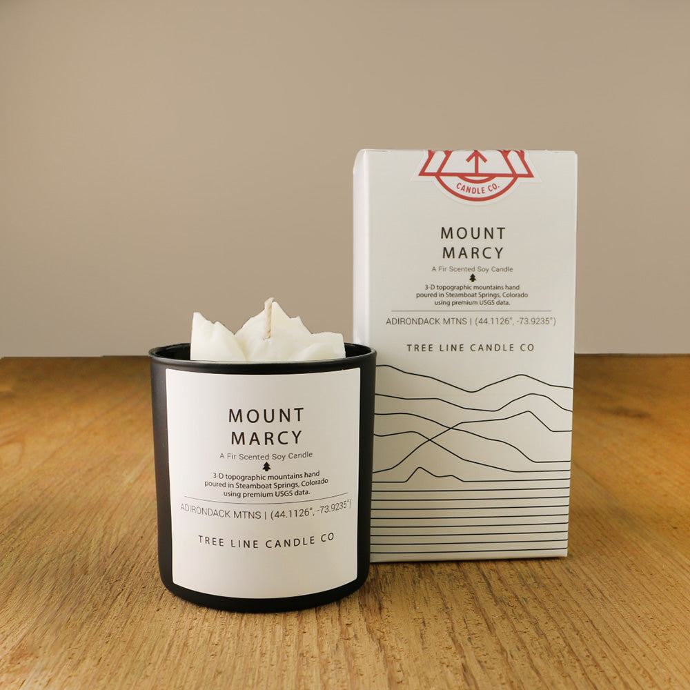 A white wax candle named Mount Marcy is next to a white box with red and black lettering.