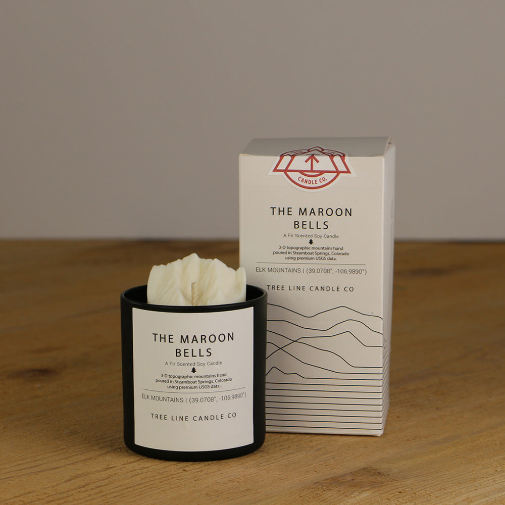 A white wax replica candle of The Maroon Bells  next to a white box with red and black lettering.