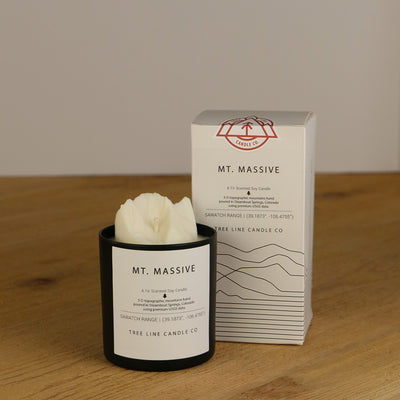 A white wax replica candle of Mount Massive next to a white box with red and black lettering.