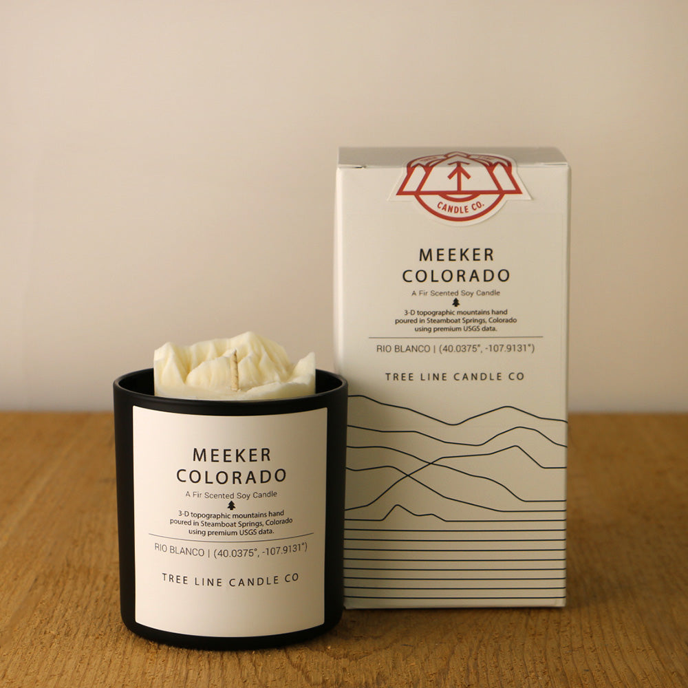 A white wax candle named Mount Meeker is next to a white box with red and black lettering.