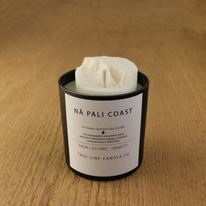 A white soy wax replica candle of Nä Pali Coast in a round, black glass.