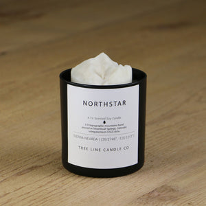 A white soy wax replica candle of Northstar in a round, black glass.
