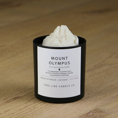 A white soy wax replica candle of Mount Olympus in a round, black glass.