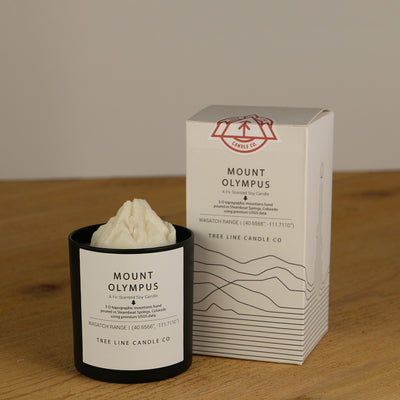 A white wax replica candle of Mount Olympus next to a white box with red and black lettering.
