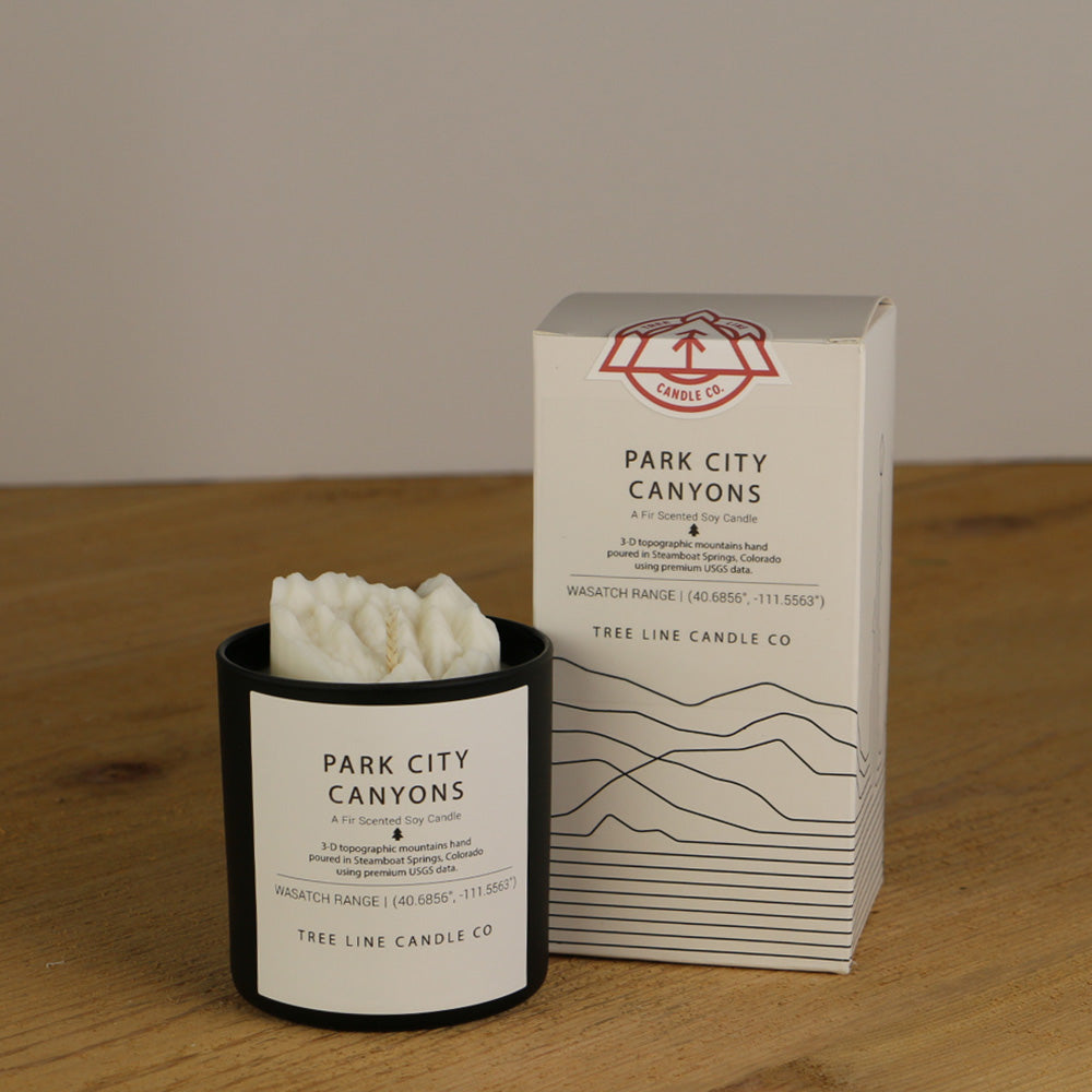 A white wax replica candle of Park City Canyons next to a white box with red and black lettering.