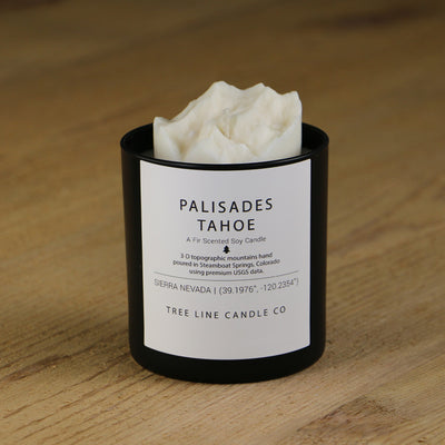 A white soy wax replica candle of Palisades Tahoe in a round, black glass.