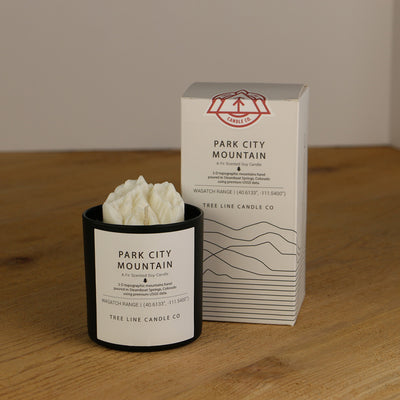 A white wax replica candle of Park City Mountain next to a white box with red and black lettering.