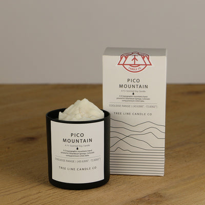 A white wax replica candle of Pico Mountain next to a white box with red and black lettering.