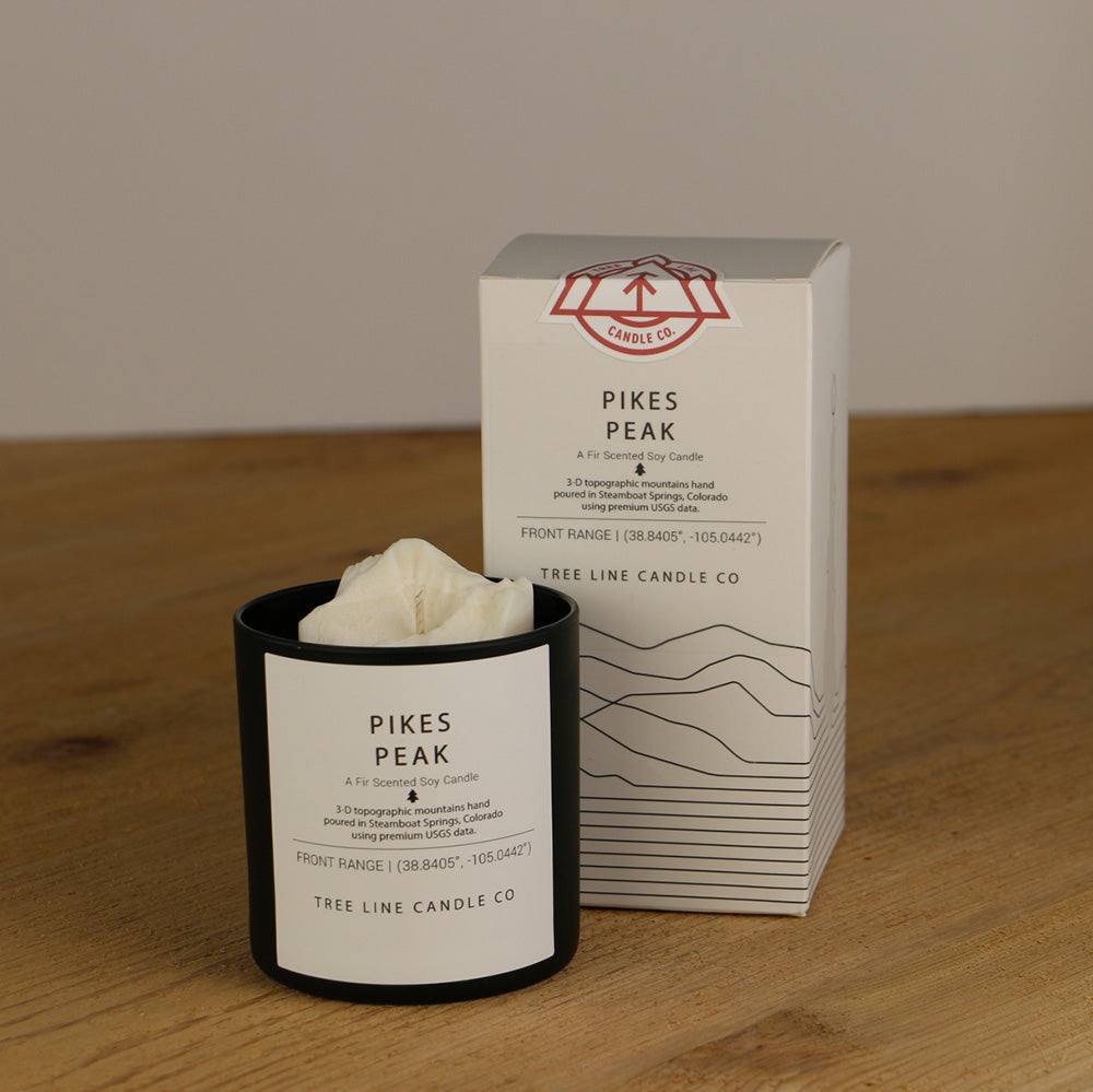 A white wax replica candle of Pikes Peak next to a white box with red and black lettering.