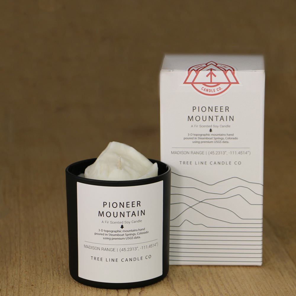 A white wax candle named Pioneer Mountain is next to a white box with red and black lettering.