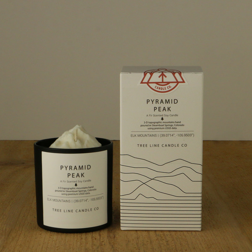 A white wax candle named Pyramid Peak is next to a white box with red and black lettering.