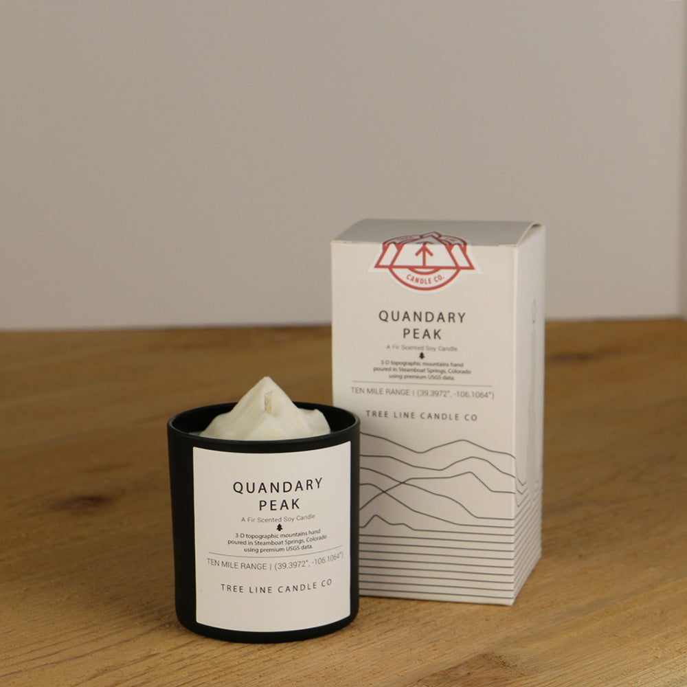 A white wax replica candle of Quandary Peak next to a white box with red and black lettering.