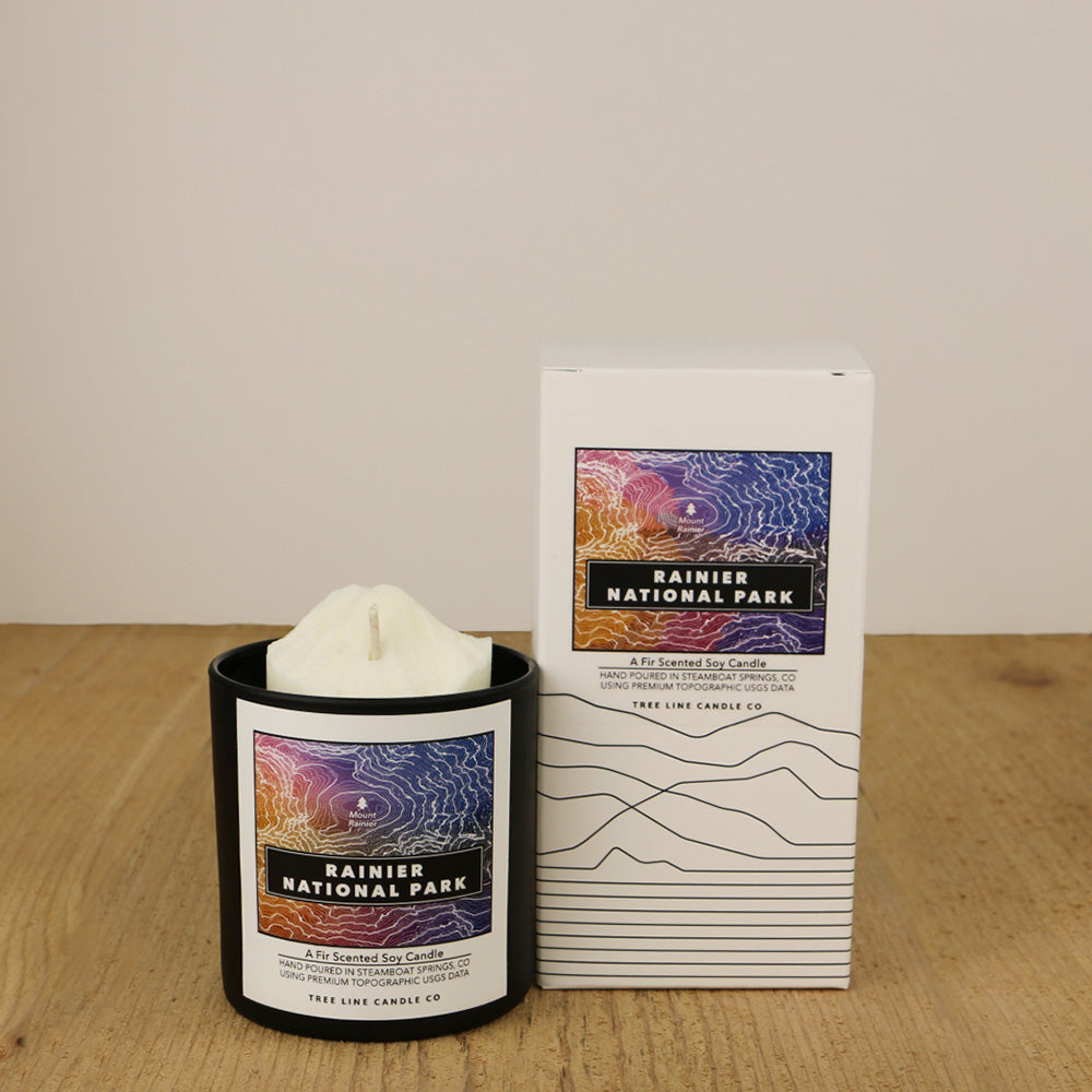 A white wax candle named Mount Rainier is next to a white box with red and black lettering.