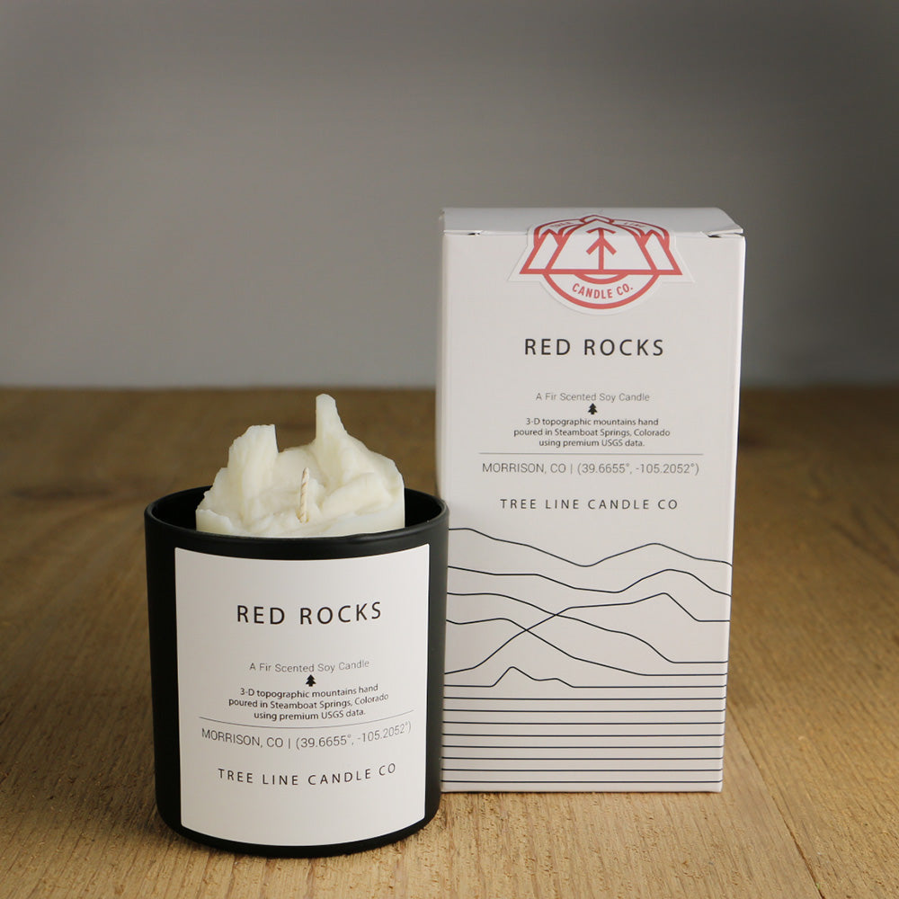 A white wax replica candle of Red Rocks next to a white box with red and black lettering.