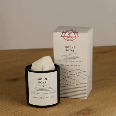 A white wax replica candle of Mount Royal next to a white box with red and black lettering.