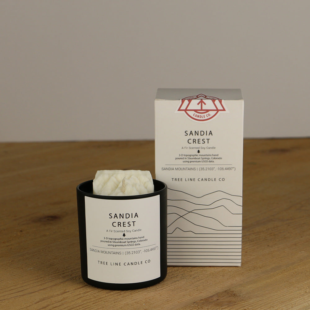 A white wax replica candle of Sandia Crest next to a white box with red and black lettering.