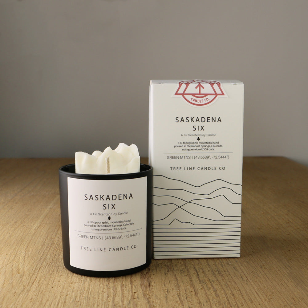 A white wax candle named Saskadena Six is next to a white box with red and black lettering.