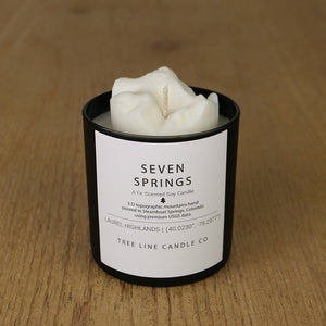  A white soy wax replica candle of Seven Springs in a round, black glass.