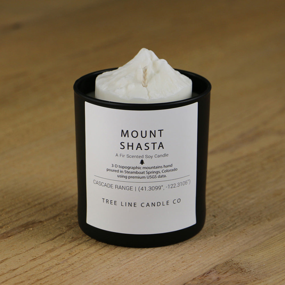 A white soy wax replica candle of Mount Shasta in a round, black glass.