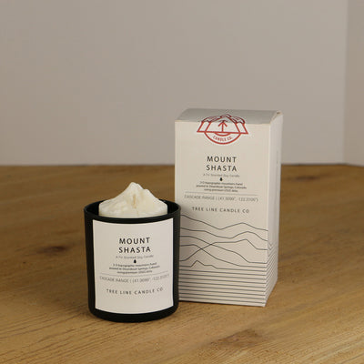 A white wax replica candle of Mount Shasta next to a white box with red and black lettering.