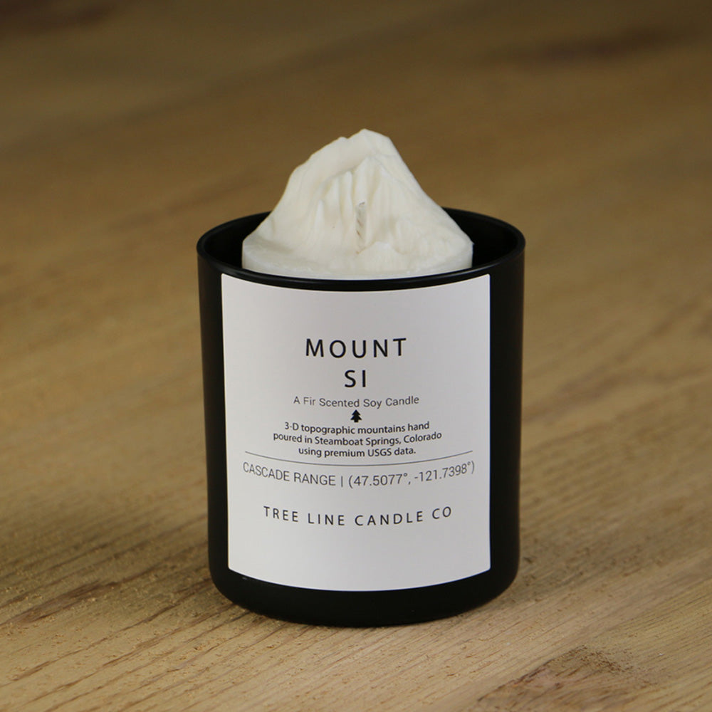 A white soy wax replica candle of Mount Si in a round, black glass.