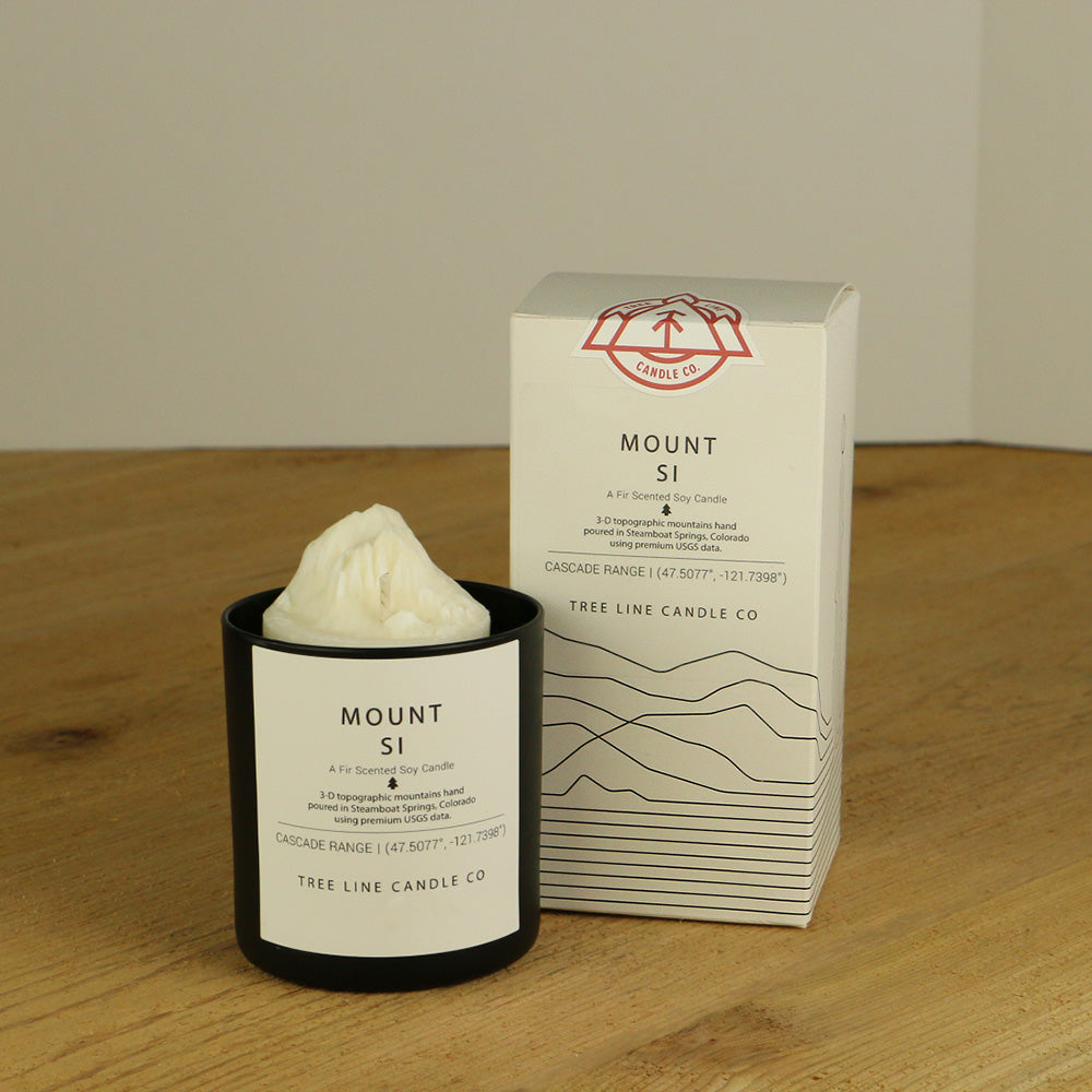 A white wax replica candle of Mount Si next to a white box with red and black lettering.