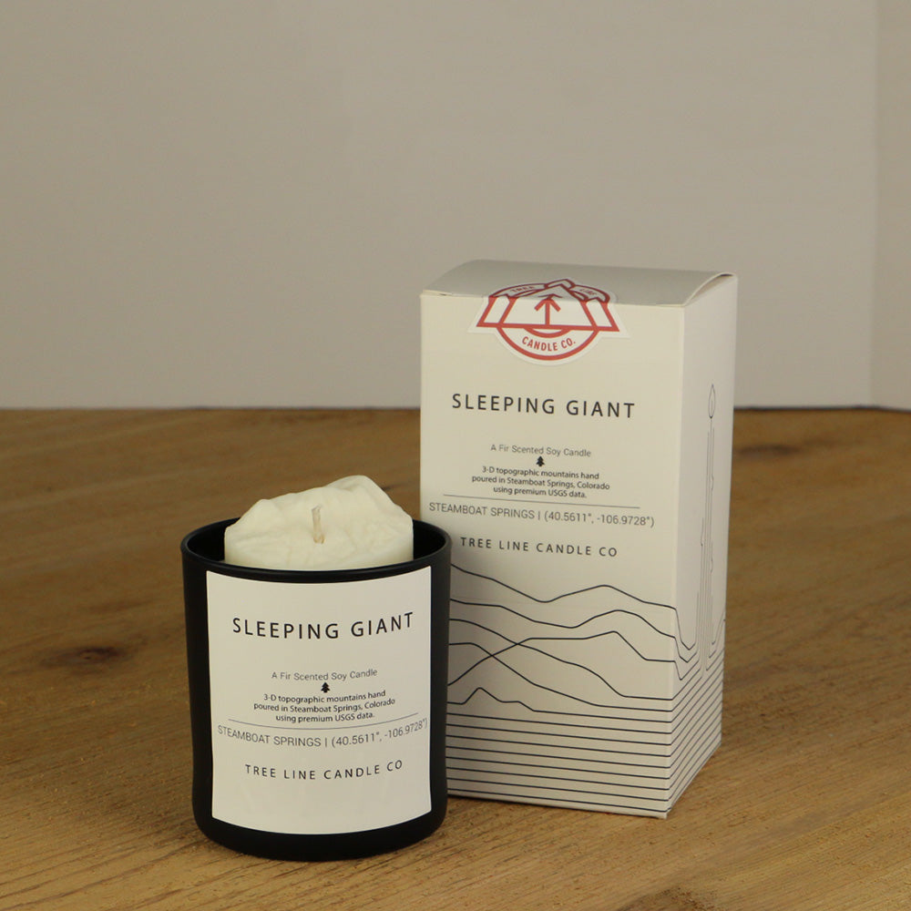 A white wax replica candle of Sleeping Giant summit next to a white box with red and black lettering.