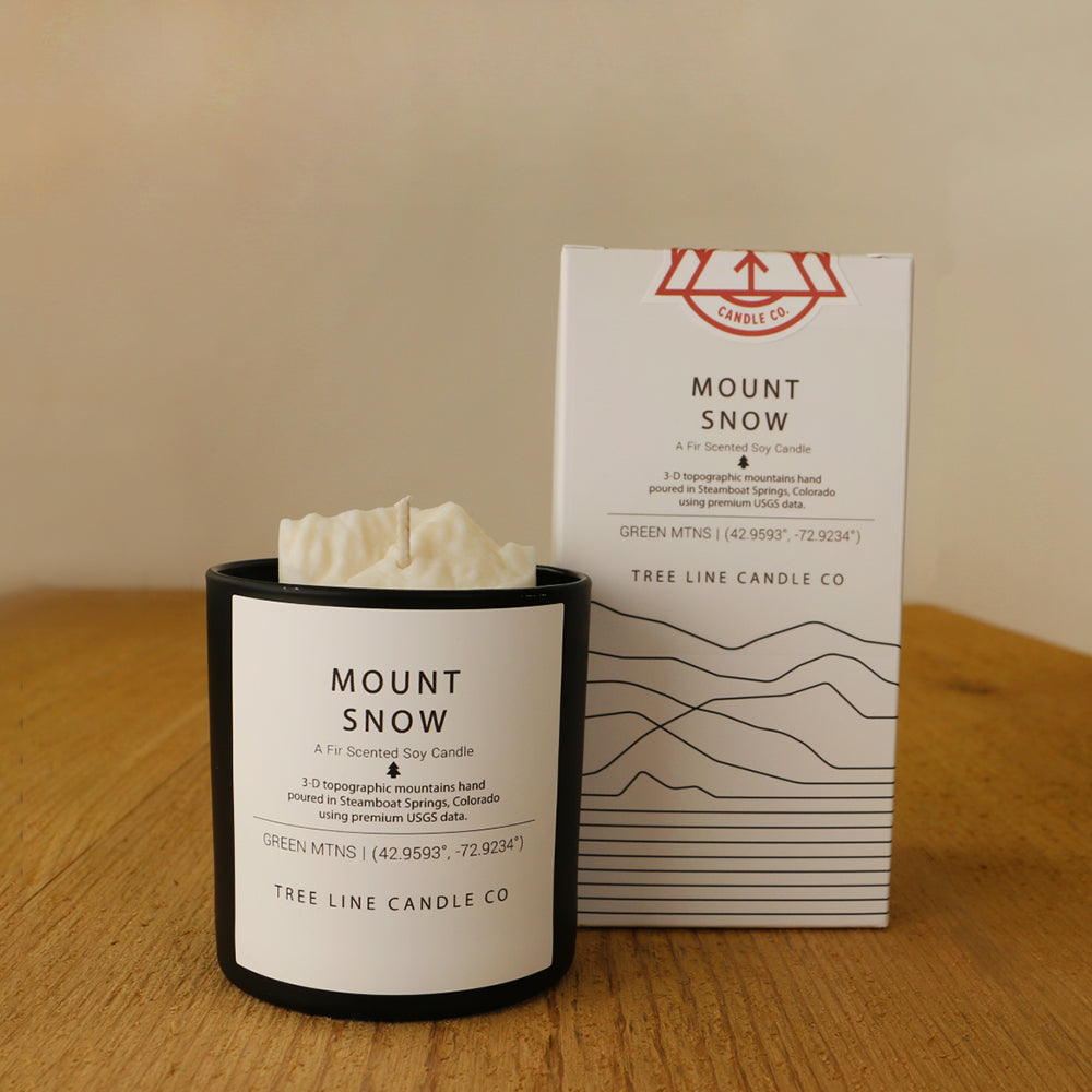 A white wax candle named Mount Snow is next to a white box with red and black lettering.