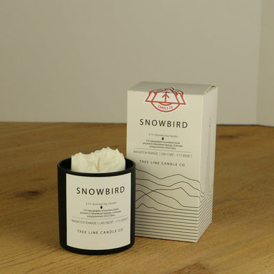 A white wax replica candle of Snowbird summit next to a white box with red and black lettering.