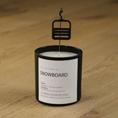  A white soy wax  candle of Snowboard candle in a round, black glass with a small black gondola chair hanging over it.