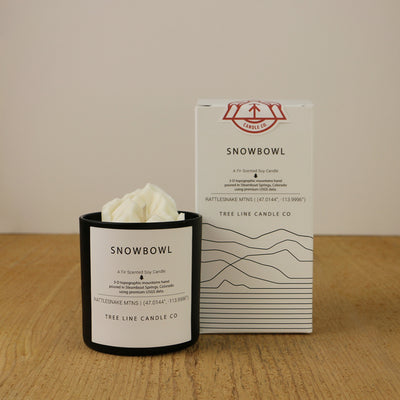 A white wax candle named Snowbowl is next to a white box with red and black lettering.