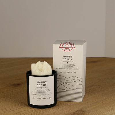 A white wax replica candle of Mount Sopris summit next to a white box with red and black lettering.
